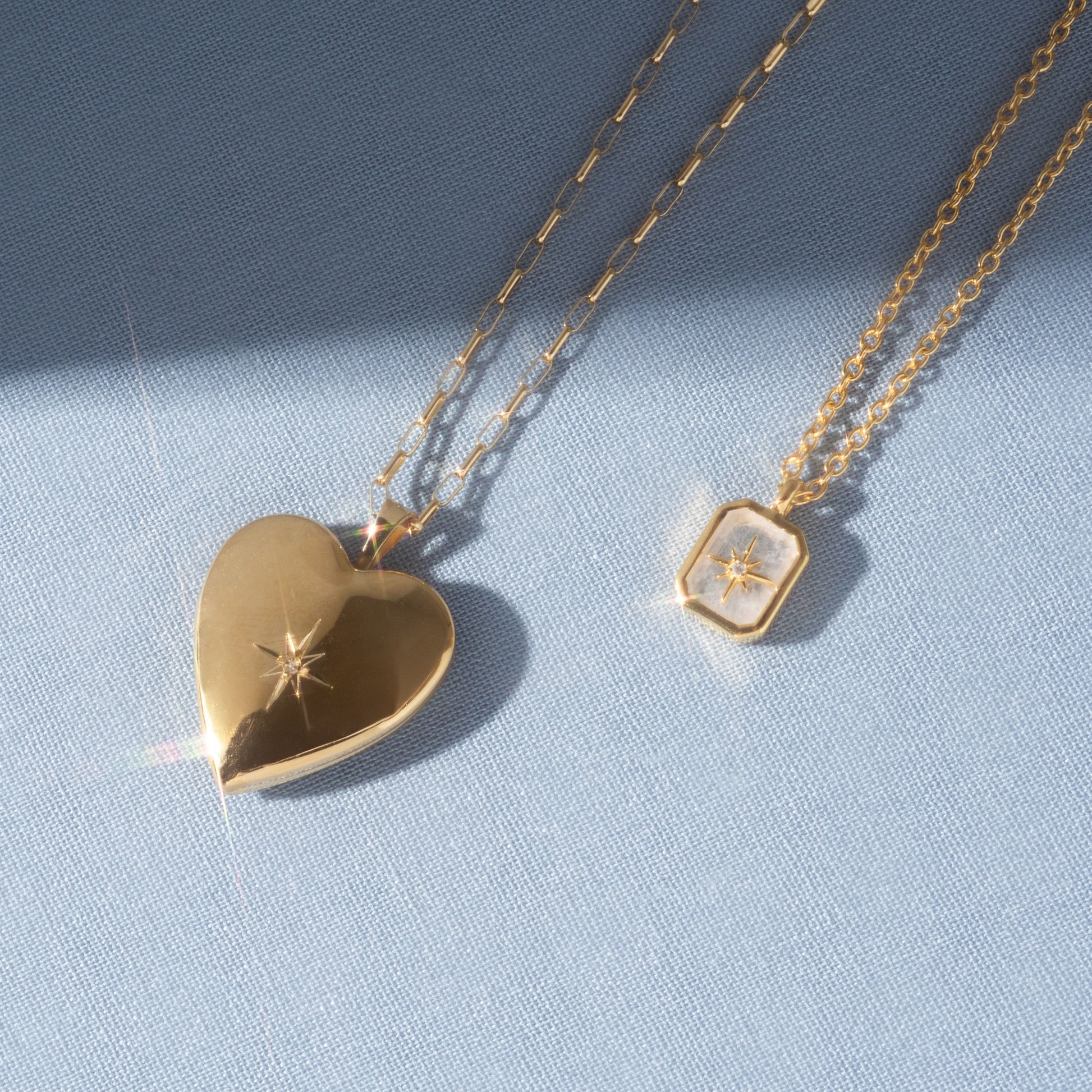 On light blue fabric: a gold Rainbow Moonstone & Diamond Manifest Your Dreams Pendant Necklace shines with a wishing star and diamond motif, both beautifully reflecting the light.