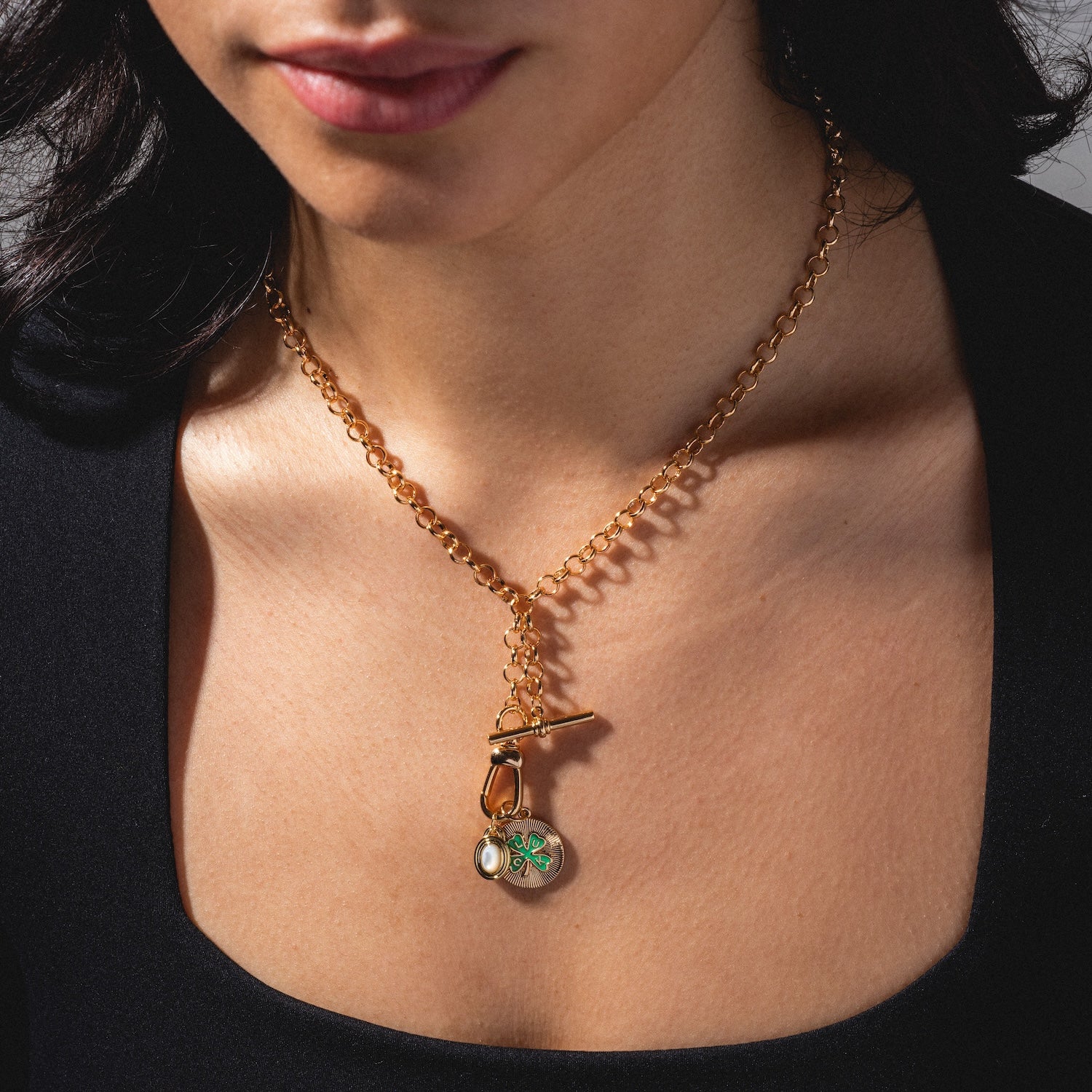 A woman models the Monroe Birthstone Charm, a gold chain necklace with a toggle clasp and a round green-and-white pendant, resting at her collarbone.