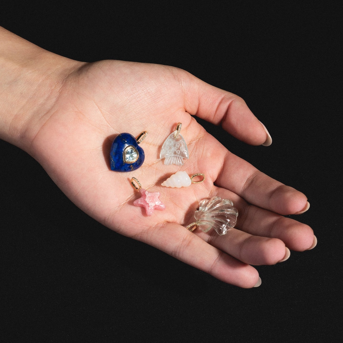 A hand holds the 14k Green Amethyst and Diamond Scallop Shell Charm against a black background, highlighting its elegant solid gold finish.