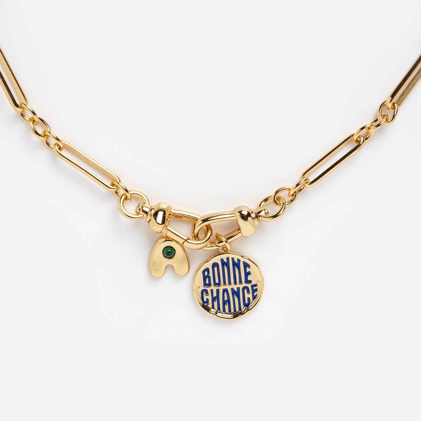The Liam Watch Chain Charm Holder Necklace features a gold chain with two charms: a gold wishbone with a green gem and a round gold pendant inscribed with BONNE CHANCE in blue.