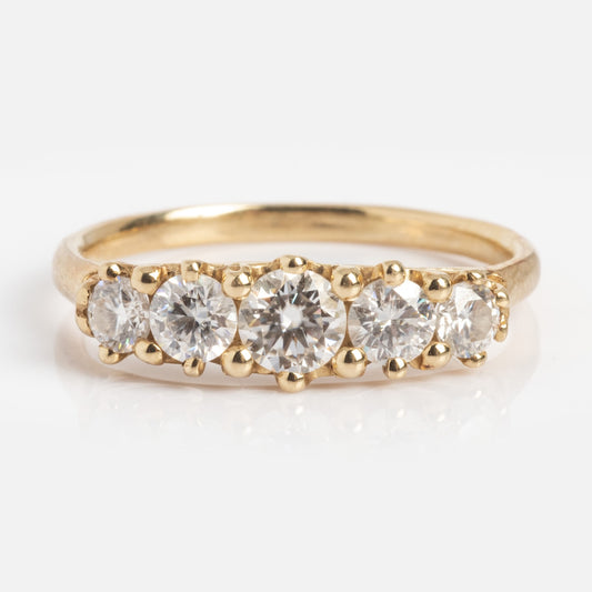 The Anniversary Band features a 1.7 mm gold band set with five round moissanite stones totaling 0.78 ctw, arranged in a row and shown from the front on a white background.