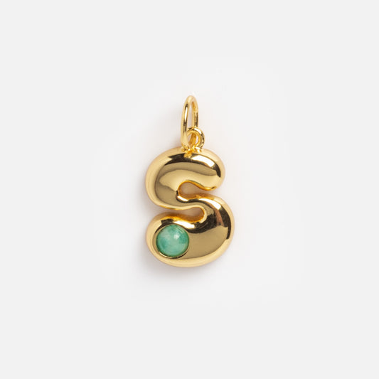 The Thea Bubble Letter Charm is a shiny gold pendant in the shape of “S,” featuring a small round green gemstone near the bottom curve, shown on a plain white background.