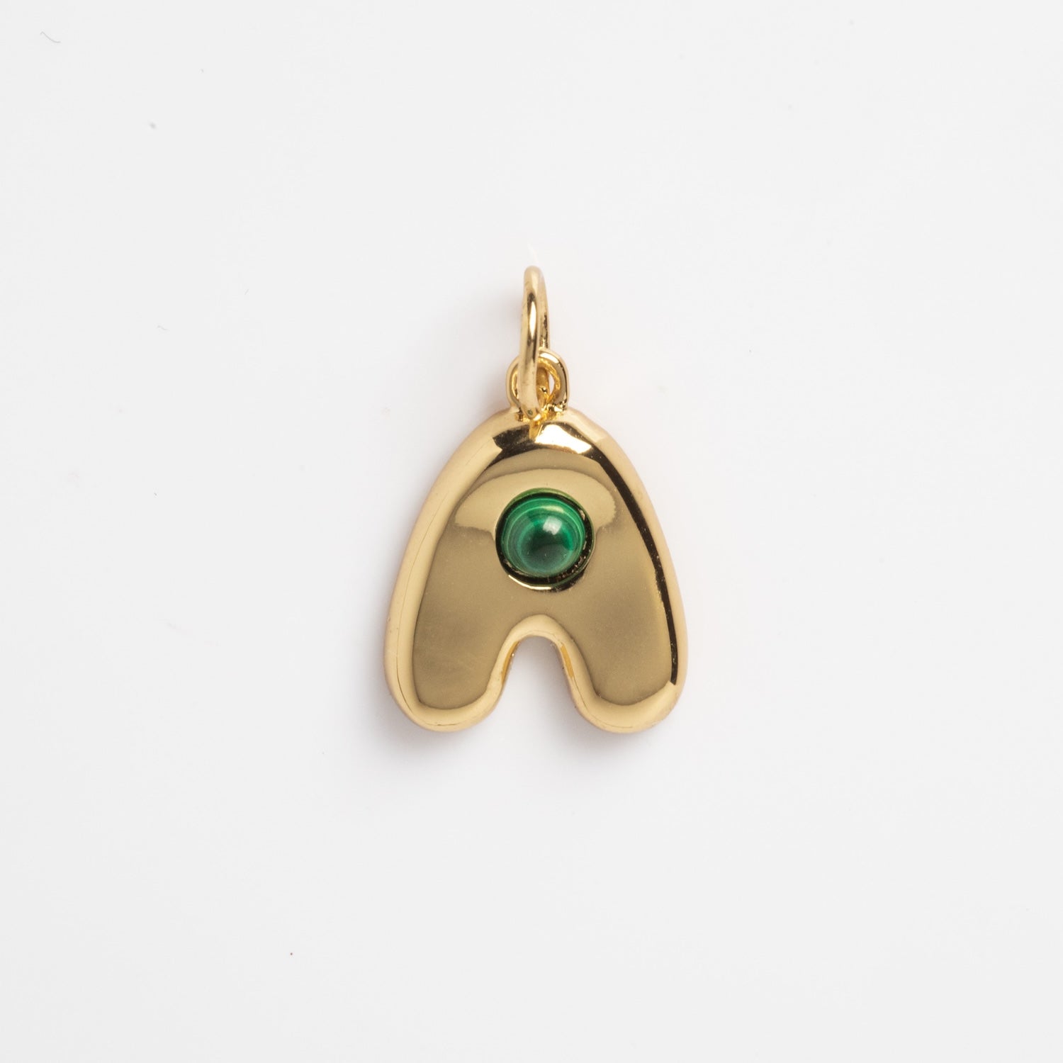 Thea Bubble Letter Charm—a gold pendant shaped like a rounded, curved "A" with a single green round gemstone set near the top center, shown against a plain white background.