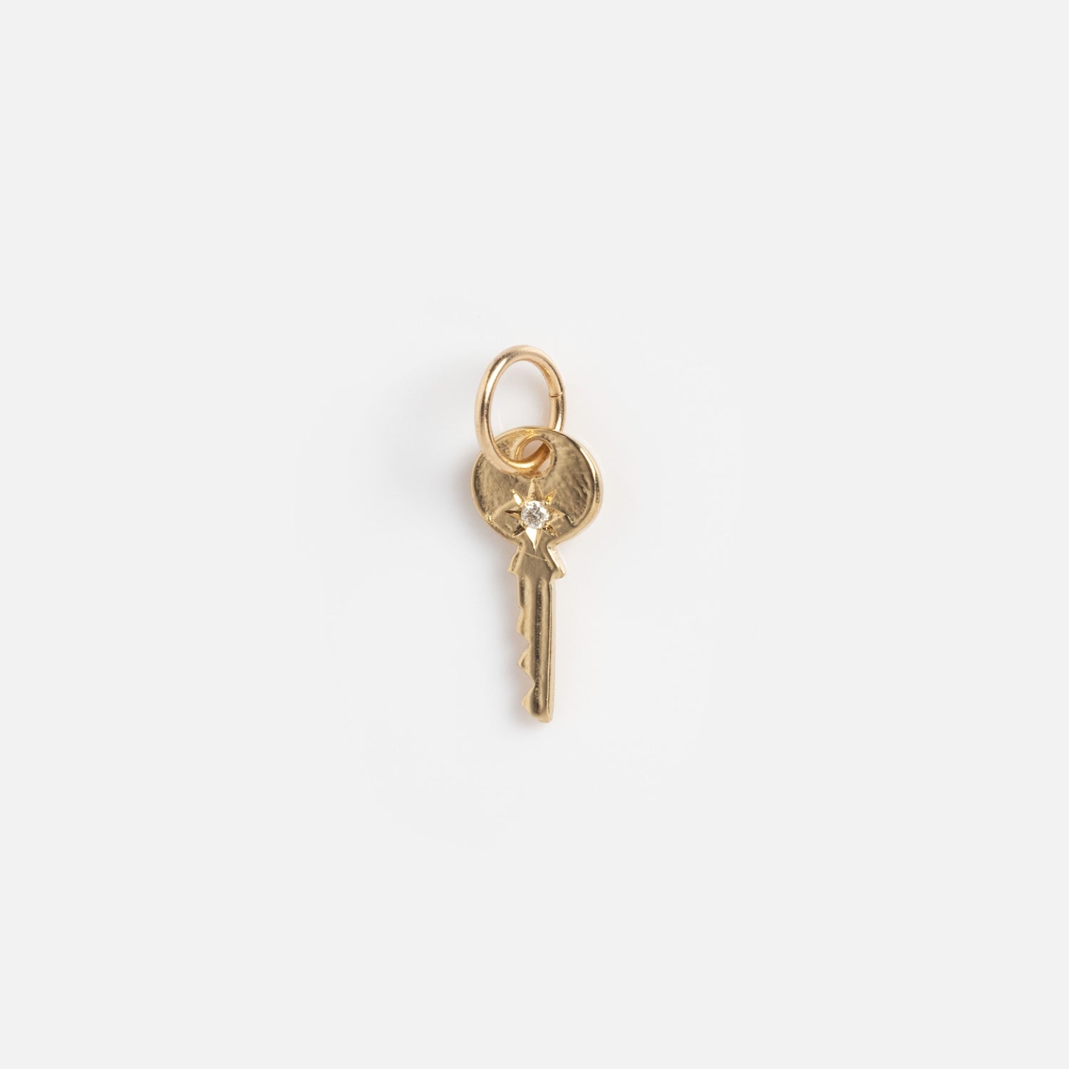 A small gold key-shaped charm from Charms by Charlie and Marcelle, featuring a top loop, displayed on a plain white background.