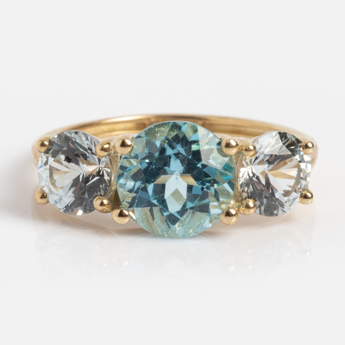 A 9k solid yellow gold pinky ring in sample size 5, featuring a trilogy design with a round aquamarine center stone flanked by two smaller clear gemstones, all set in classic four-prong settings.