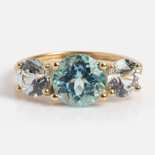 A 9k solid yellow gold pinky ring in sample size 5, featuring a trilogy design with a round aquamarine center stone flanked by two smaller clear gemstones, all set in classic four-prong settings.
