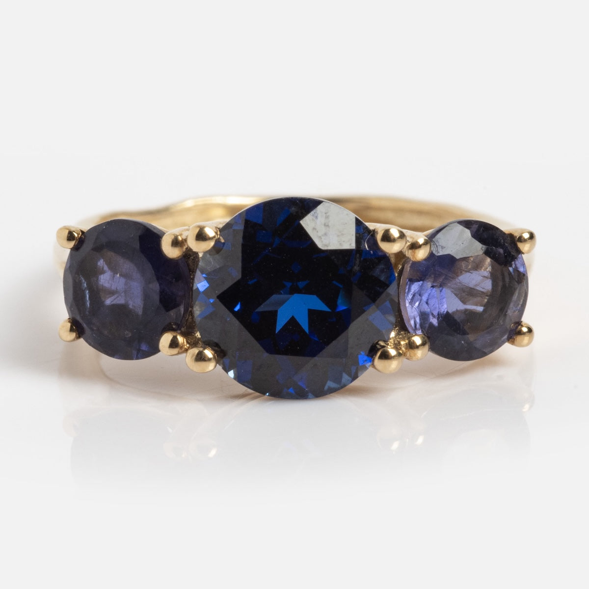 The Solid Gold Trilogy Birthstone Pinky Ring Blue Sapphire (Sample Size 5) is a 9k yellow gold ring with three round blue stones—a central lab sapphire between two smaller ones—shown on a plain white background.