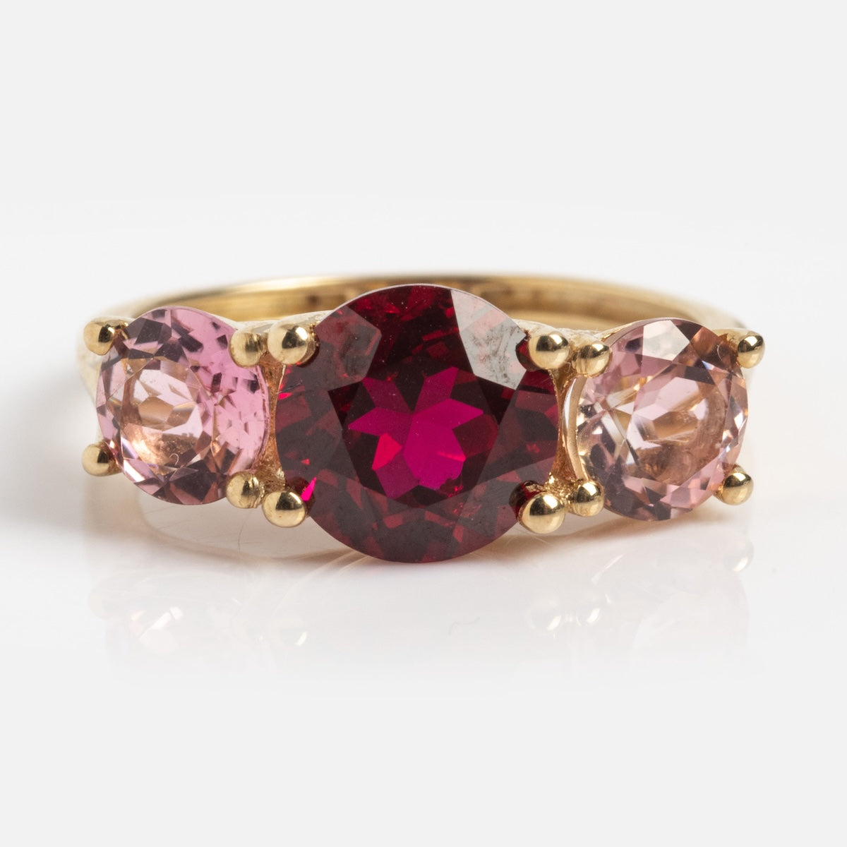 The Solid Gold Trilogy Birthstone Pinky Ring Ruby Sample Size 5 features a large round lab ruby center and two smaller pink tourmalines in 9k solid yellow gold, set on a plain white background.