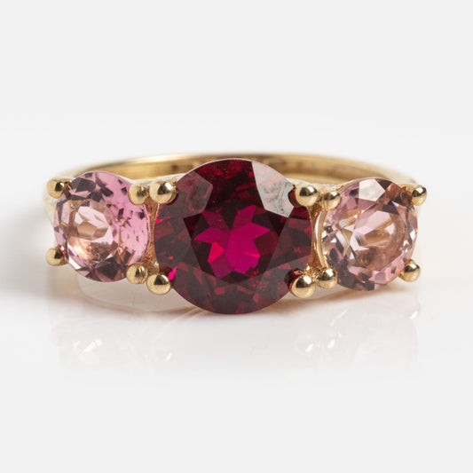 The Solid Gold Trilogy Birthstone Pinky Ring Ruby Sample Size 5 features a large round lab ruby center and two smaller pink tourmalines in 9k solid yellow gold, set on a plain white background.