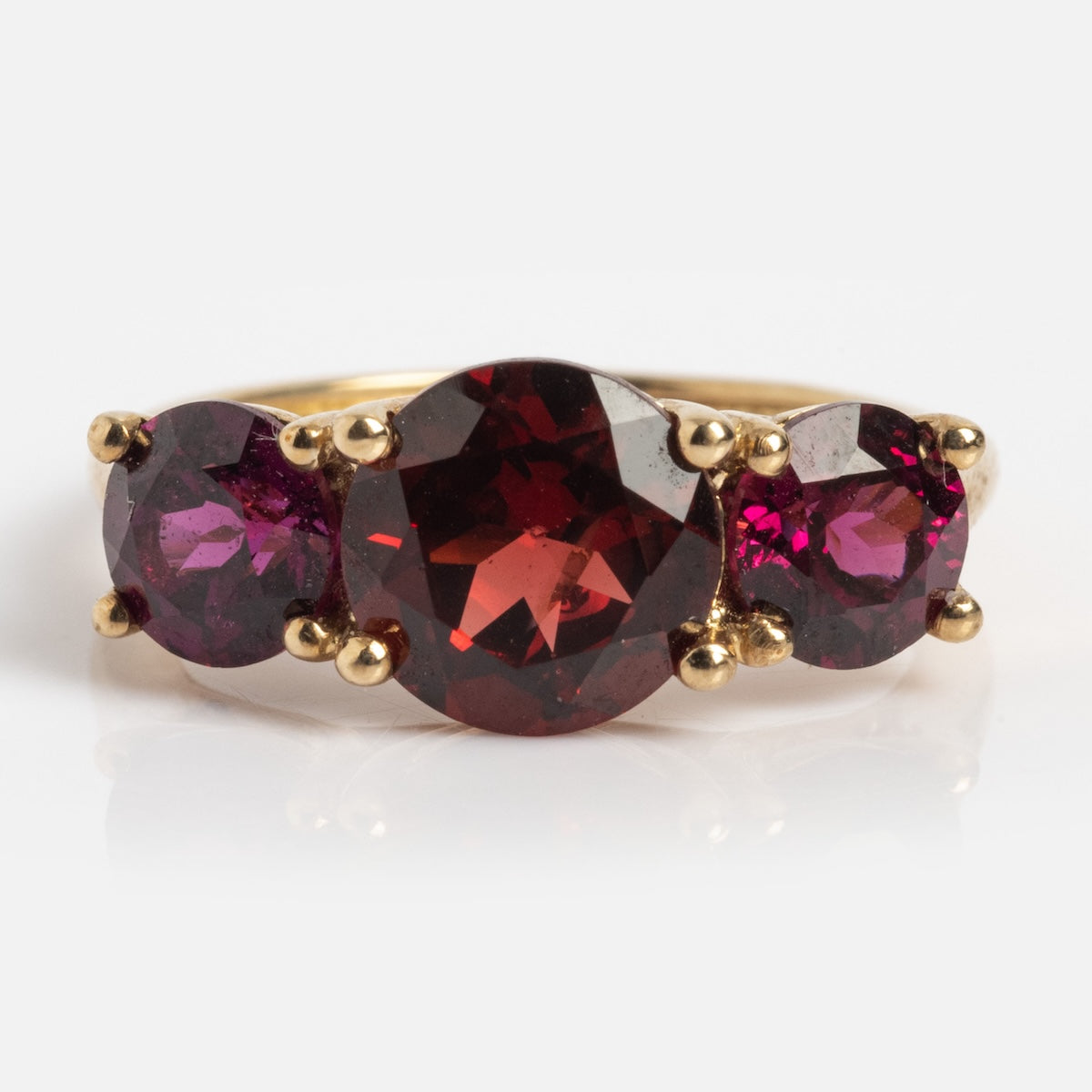 The Solid Gold Trilogy Birthstone Pinky Ring in size 5 showcases three prong-set round garnets, with a larger central stone, all set in yellow gold and displayed on a white background.