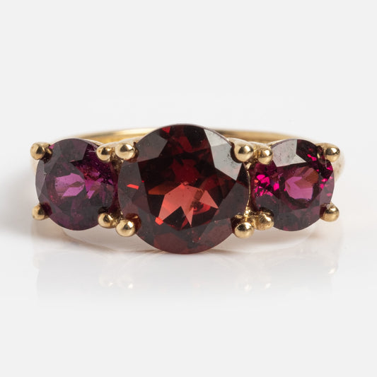 The Solid Gold Trilogy Birthstone Pinky Ring in size 5 showcases three prong-set round garnets, with a larger central stone, all set in yellow gold and displayed on a white background.