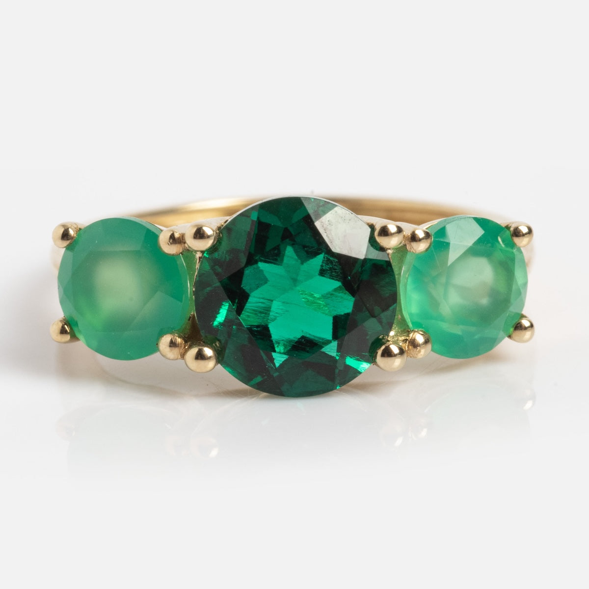 The Solid Gold Trilogy Birthstone Pinky Ring (Emerald, Size 5) features three round lab emeralds—one large center stone and two smaller side stones—set in 9k solid yellow gold prongs, shown against a white background.