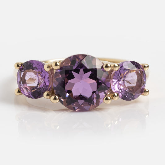 The Solid Gold Trilogy Birthstone Pinky Ring (Amethyst, Size 5) features three round purple gemstones with a larger center stone, shown against a white background.