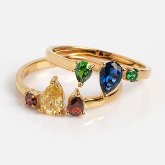The Interlocking Gem Ring Set Sample Size 7 features two 14k yellow gold plated rings with red, yellow, green, and blue CZ stones in various cuts and sizes for a striking multicolor look.