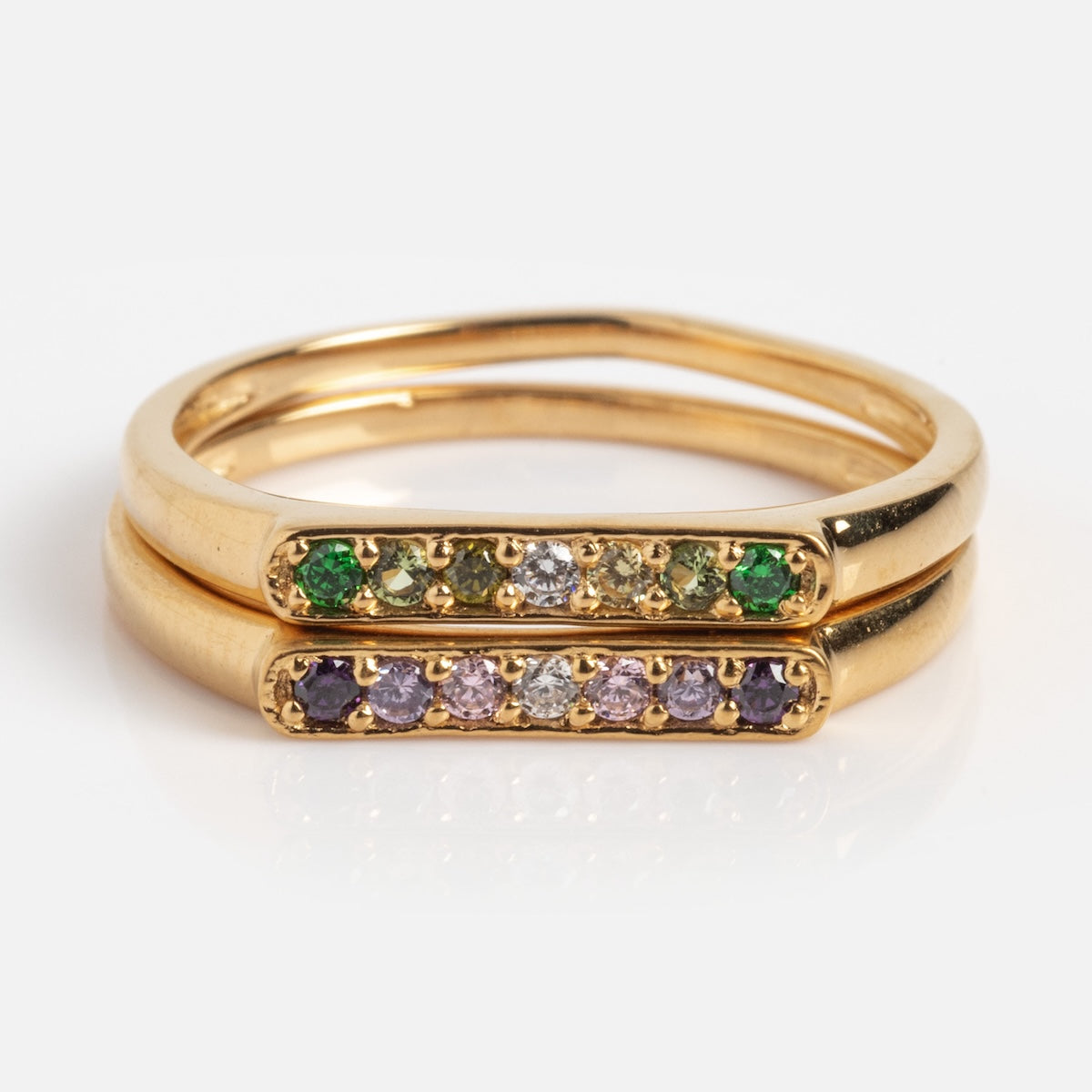 The Golden Pave Open Front Band in size 7 features two 14k yellow gold plated brass rings stacked together, each with a horizontal bar set with white CZ and colored gemstones—one green and white, the other purple and white.