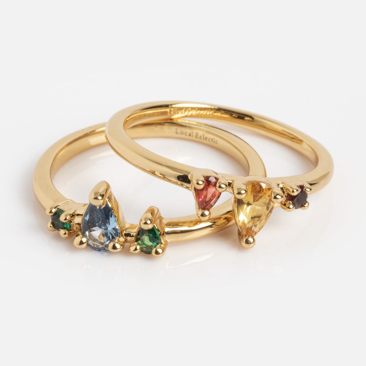 The Interlocking Color Ring Set Sample Size 5 features two 14k yellow gold plated rings with teardrop and round spinel gemstones in blue, green, red, yellow, and purple, elegantly displayed on a white background.