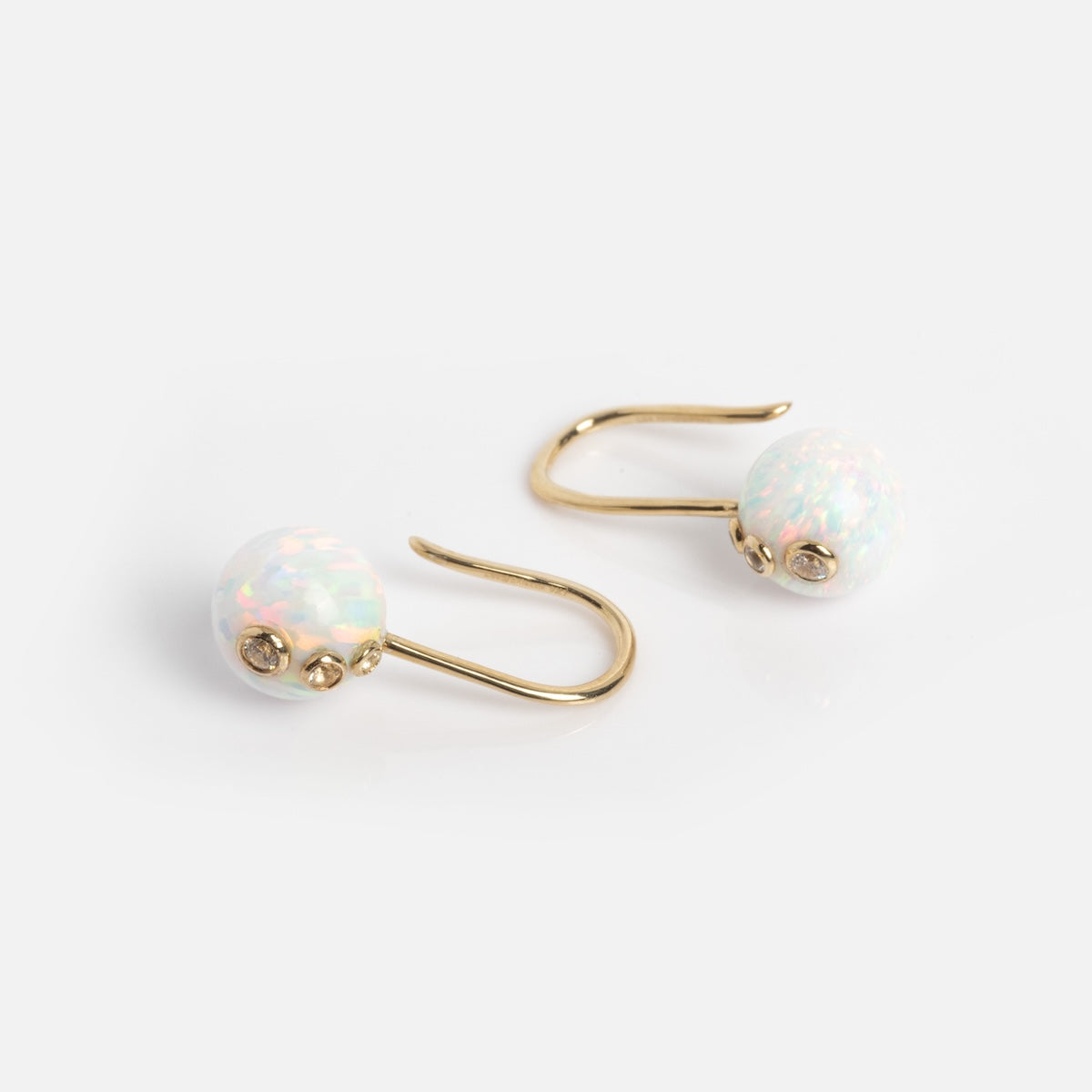 The Solid Gold Opal Drop Earrings Sample features round, iridescent synthetic opals with pink and green reflections set in 9k solid gold hooks, displayed on a plain white background.