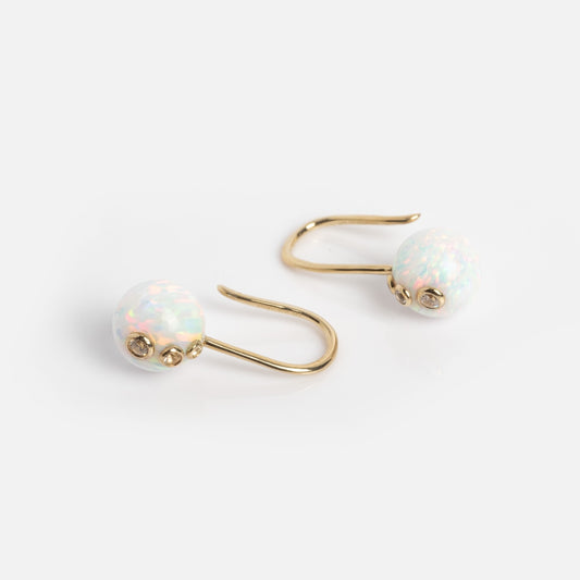The Solid Gold Opal Drop Earrings Sample features round, iridescent synthetic opals with pink and green reflections set in 9k solid gold hooks, displayed on a plain white background.