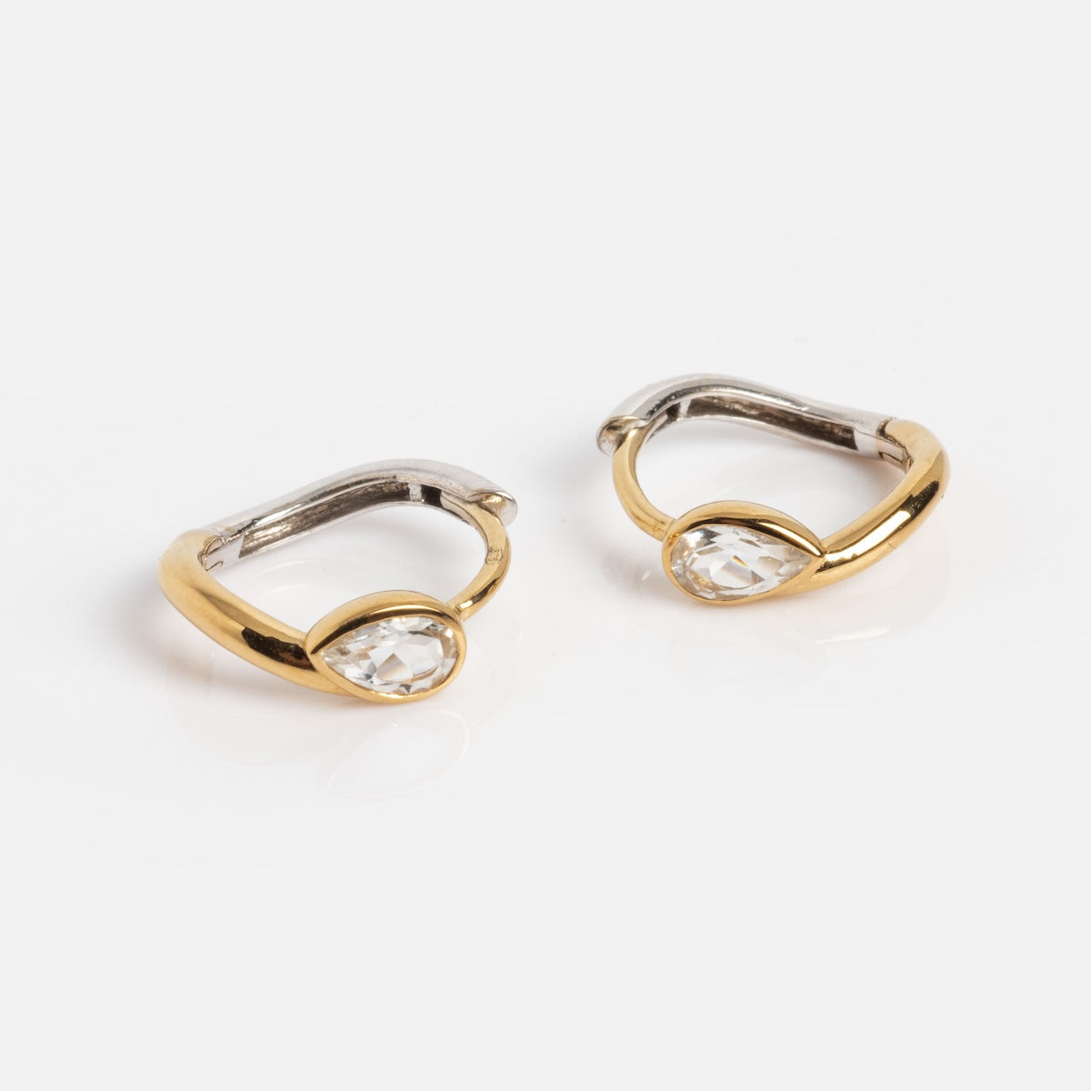 The Solid Gold Two Tone Topaz Huggie Hoops Sample features small hoops in gold and silver tones, each with a 3x5 mm pear cut white topaz in a modern, minimalist design, displayed on a white background.