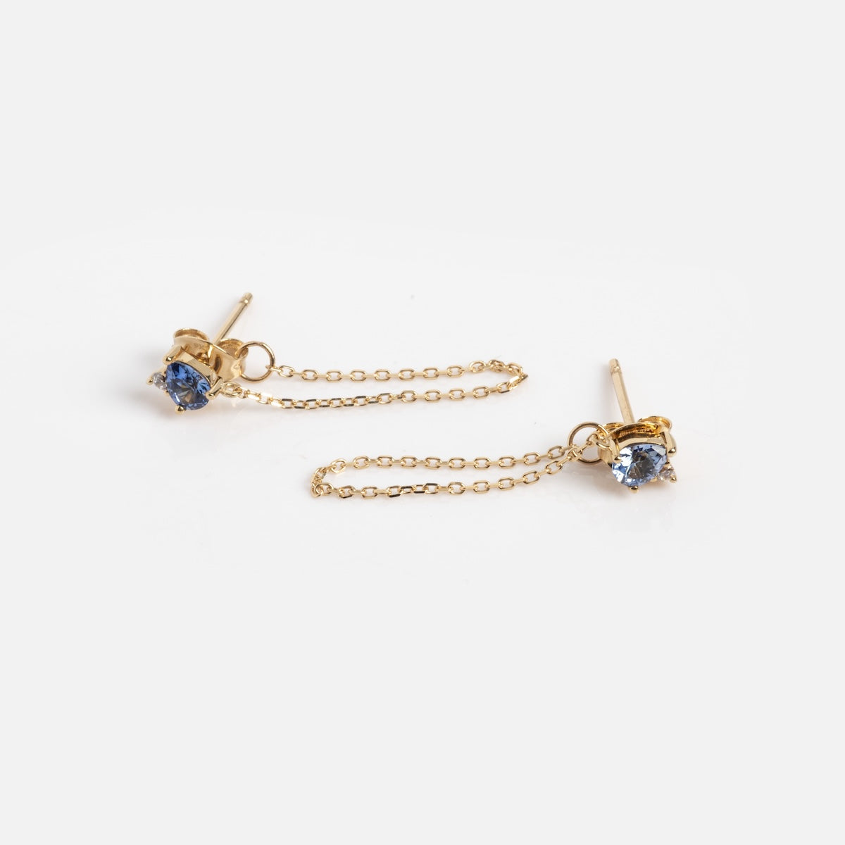 Introducing the Solid Gold Tanzanite Drop Earrings Sample: gold stud earrings with lab tanzanite gemstones, each linked by a delicate 9k solid gold chain, shown on a white background.