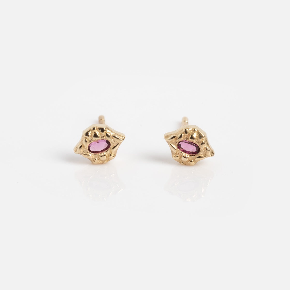 The Solid Gold Garnet Earrings Sample features a pair of small 9k gold studs with an irregular organic shape and a pink oval gemstone at the center, shown on a plain white background.