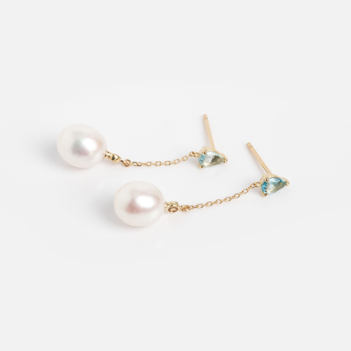 The Solid Gold Blue Topaz and Pearl Drop Earrings Sample features 9k gold drops with small Swiss Blue Topaz studs and large round white pearls on delicate chains, shown against a plain white background.