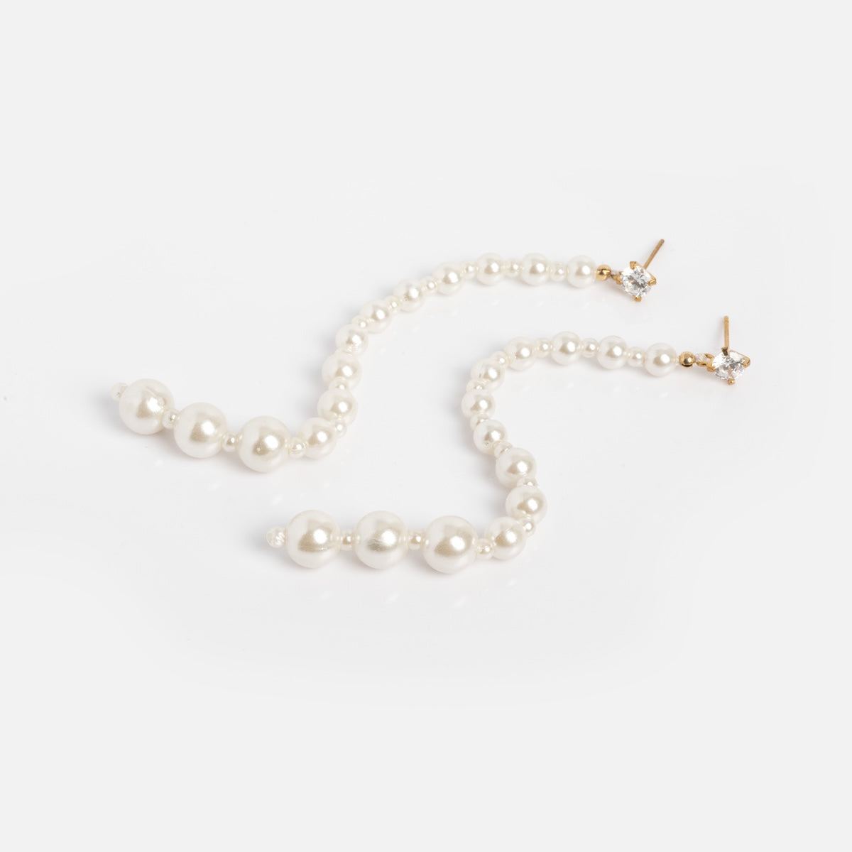 The Miami Vice Earrings Sample features long, dangling earrings with graduated white pearls and 14k vermeil posts accented by small sparkling stones, shown arranged on a plain white background.