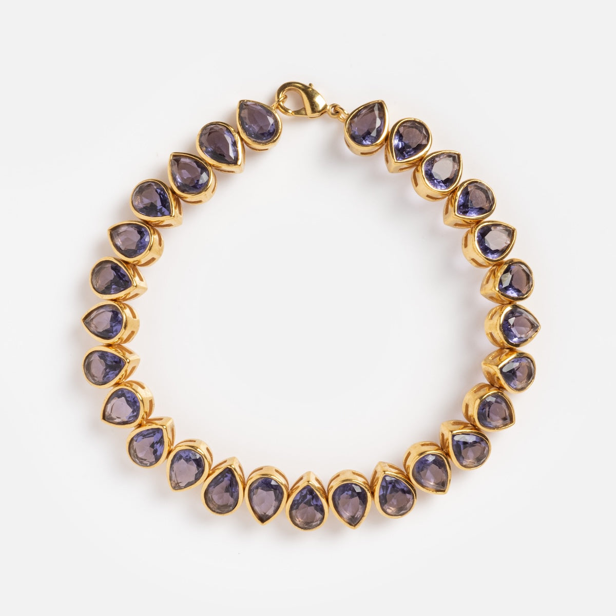 The Bezel Set Birthstone Tennis Bracelet February Sample features teardrop-shaped purple cubic zirconia gemstones in yellow gold-plated bezels, evenly spaced along the chain and displayed on a plain white background.