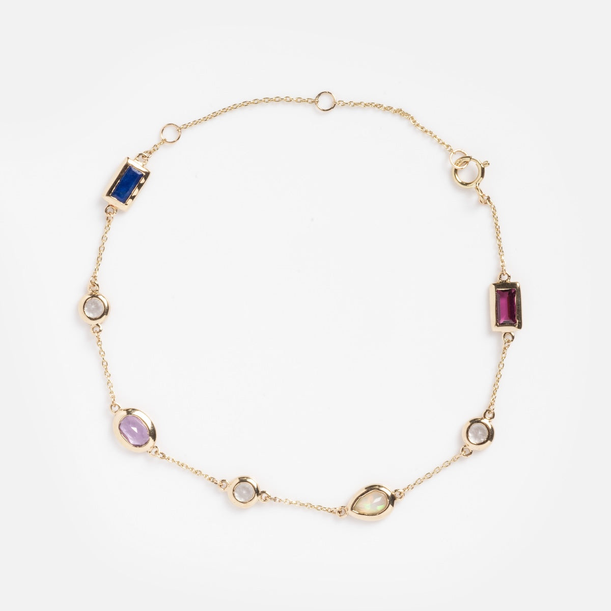The Solid Gold Love Acrostic Bracelet Sample is a delicate 9k gold chain adorned with oval and rectangular gemstones—amethyst, opal, blue, red, green, and white—elegantly spaced throughout.