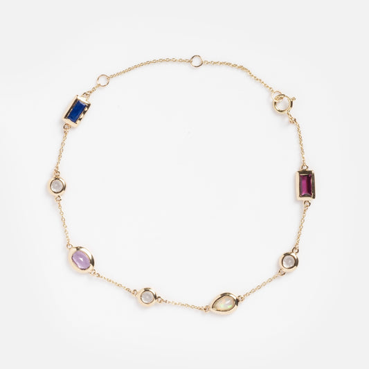 The Solid Gold Love Acrostic Bracelet Sample is a delicate 9k gold chain adorned with oval and rectangular gemstones—amethyst, opal, blue, red, green, and white—elegantly spaced throughout.