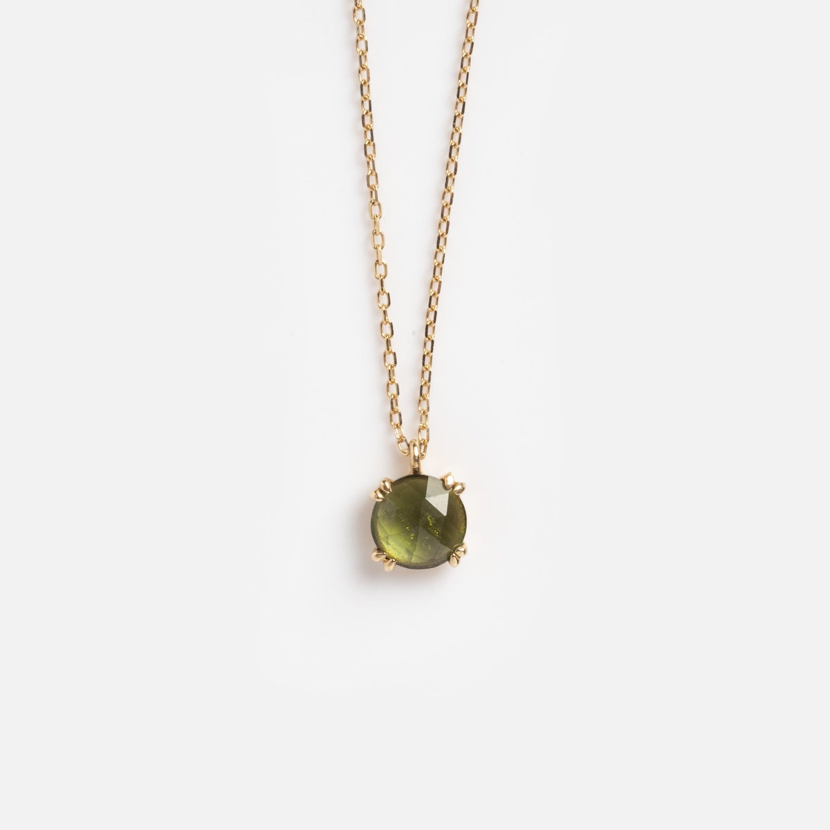 The Solid Gold Shimmering Gemstone Pendant Necklace Green Tourmaline Sample features a faceted green tourmaline pendant in a 14k yellow gold prong setting, displayed on a plain white background.