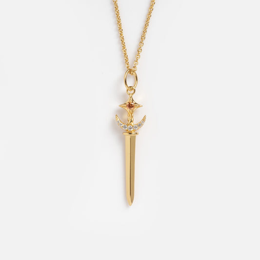 The Dagger Necklace Sample is a 14k gold plated necklace with a brass sword-shaped pendant, featuring a crescent moon and star at the top and accented with small white CZ gemstones above the blade.