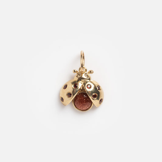 The Solid Gold Lady Bug Charm Sample features a ladybug design in solid yellow gold, with small dark spots on its wings and a sparkling garnet center, shown against a plain white background.