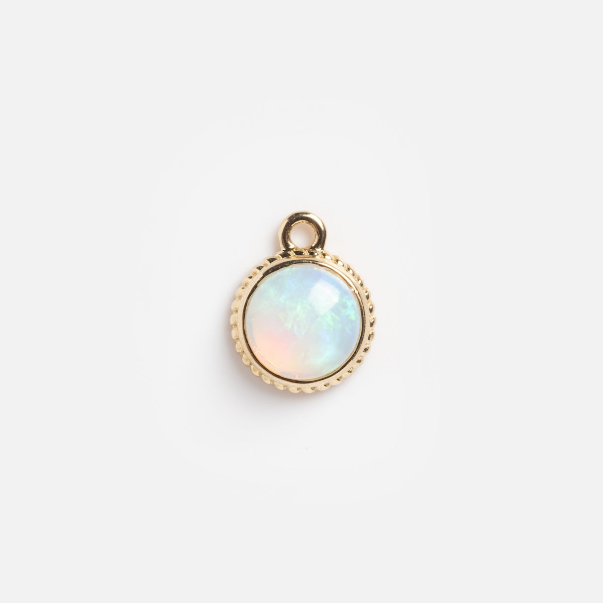 A Solid Gold Bezeled Opal Cabochon Charm Sample with a round opal set in gold bezel and a small top loop, shown on a plain white background.