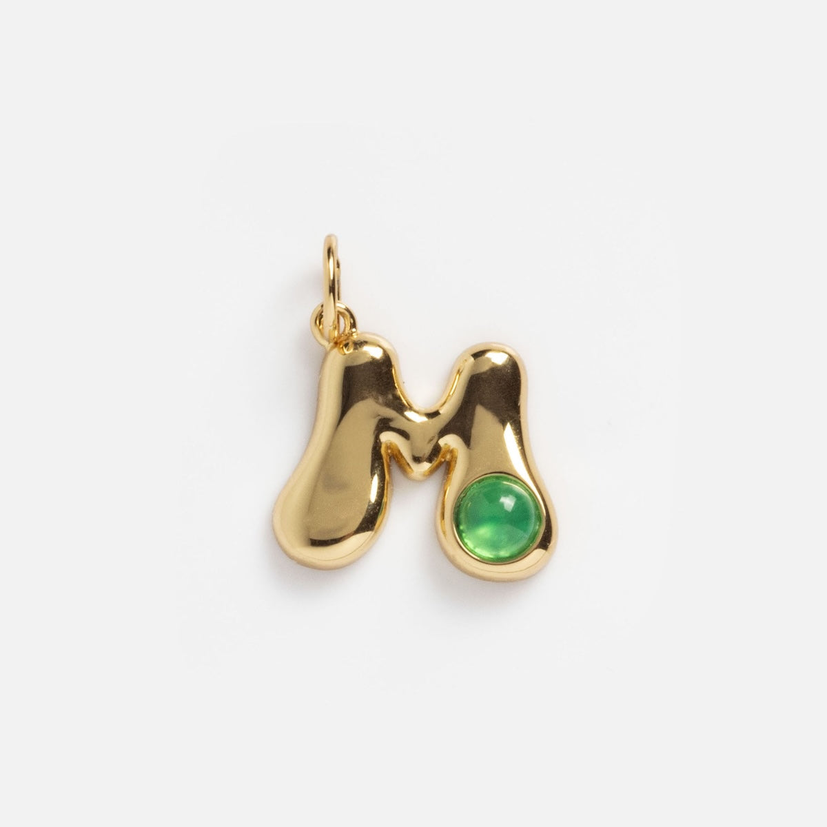 The Thea Bubble Letter Charm is a shiny gold “M” with a round green gemstone at the bottom right, hanging from a small loop against a plain white background.