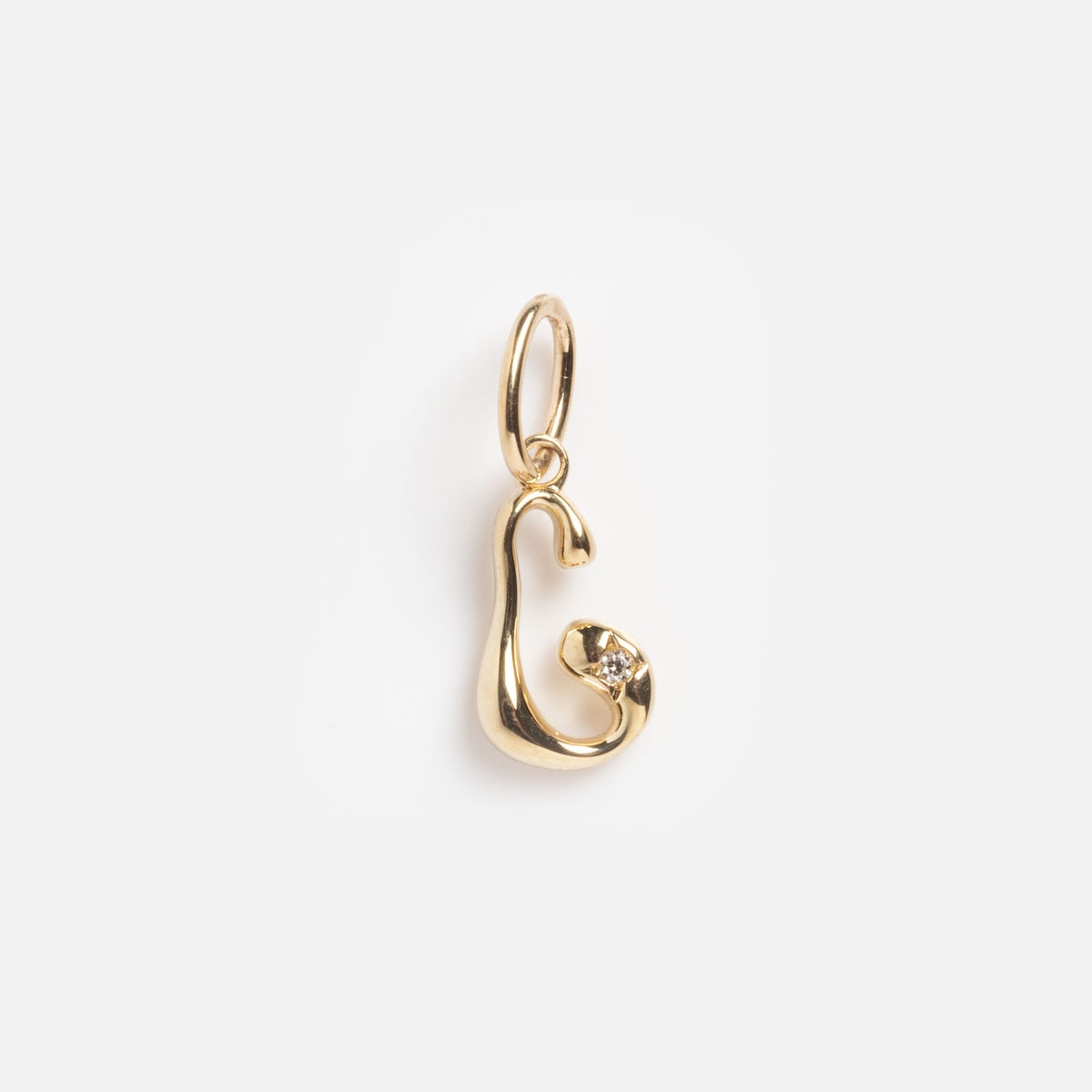 The Solid Gold Wavy Monogram Charm 'C' Sample features an abstract, curved gold design with a shiny finish, a small embedded gemstone near the bottom, and a gold loop for easy hanging.