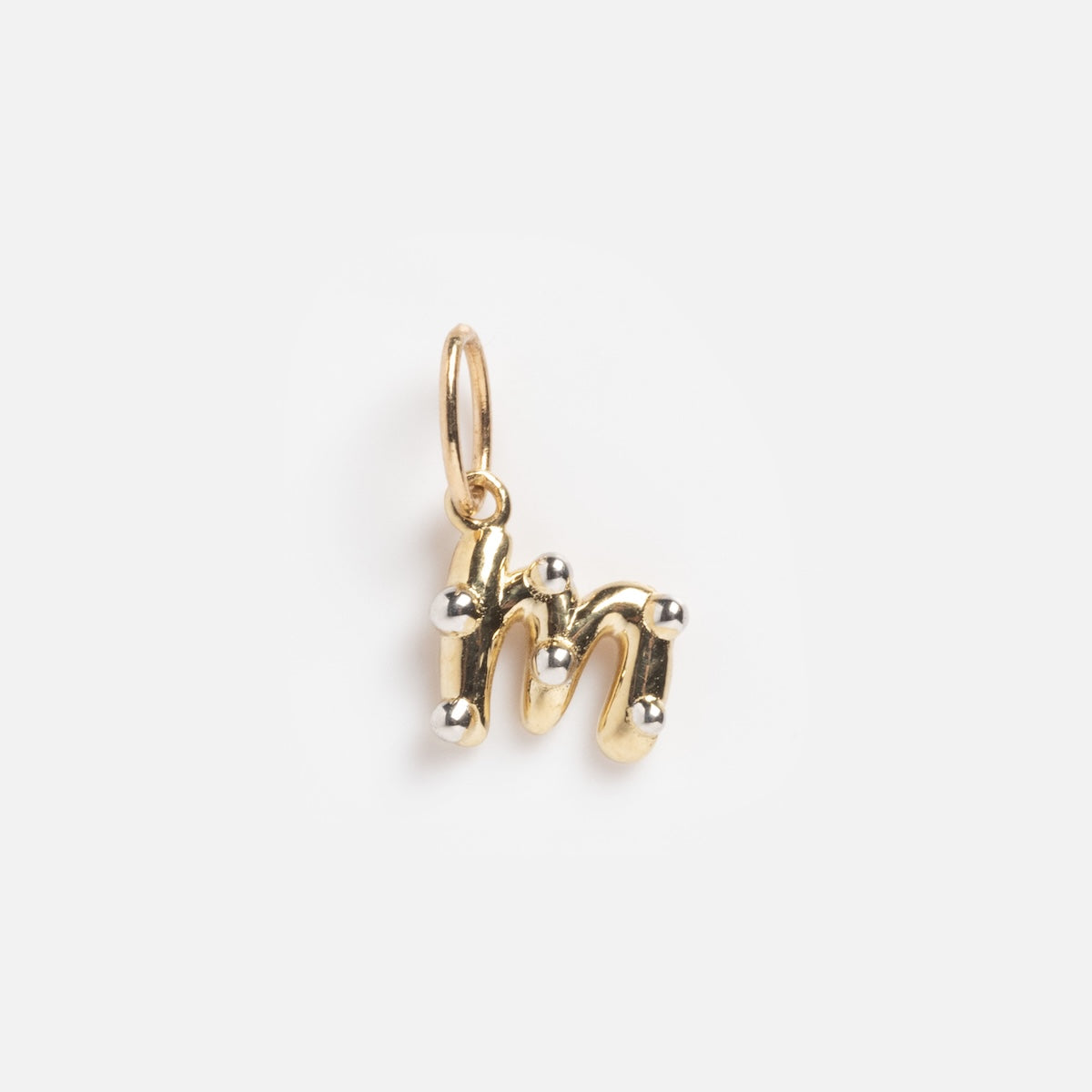 The Solid Gold Mixed Metal Monogram Charm 'M' Sample is a small gold pendant shaped like a lowercase 'm', featuring rounded edges, silver ball accents, and a top loop for attaching to a chain.