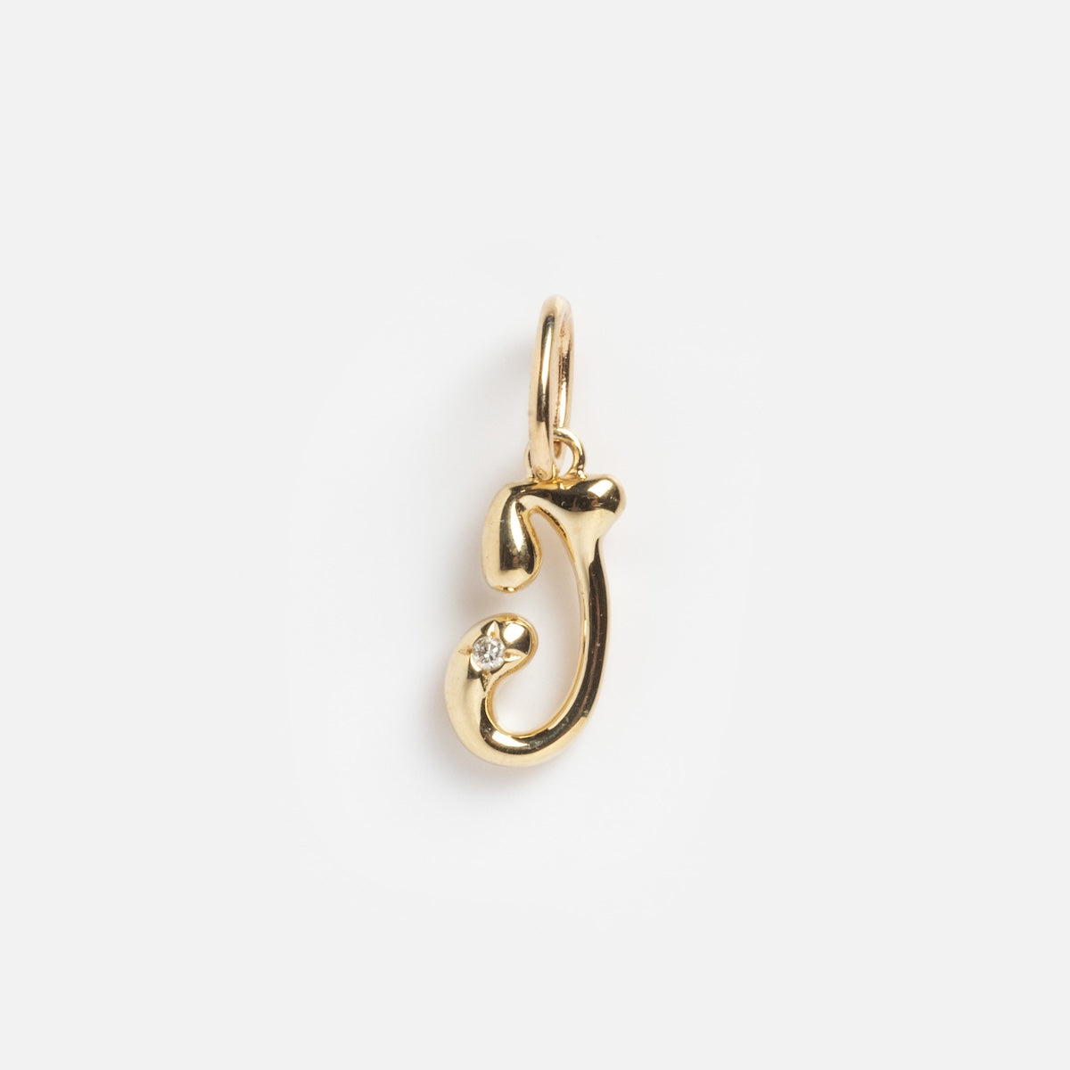 The Solid Gold Wavy Monogram Charm 'J' Sample is a gold pendant shaped like the letter J, featuring a small gemstone near the base, shown on a plain white background.