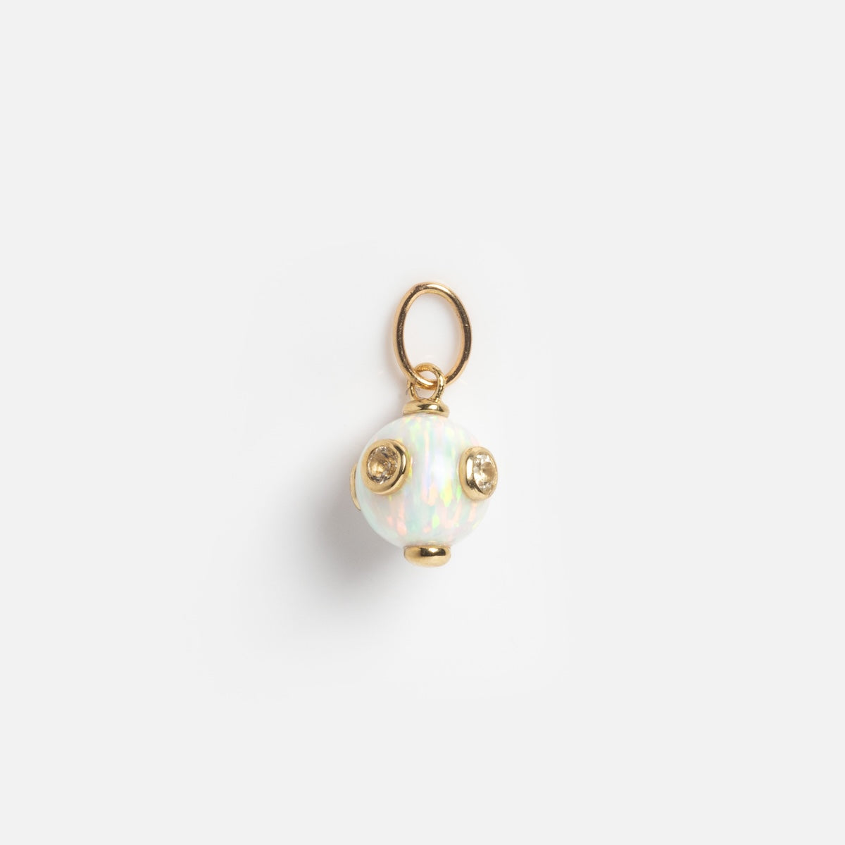 The Solid Gold Opal Gem Drop Charm Sample is a small, round opalescent charm featuring three gold studs and a gold loop at the top, shown against a plain white background.
