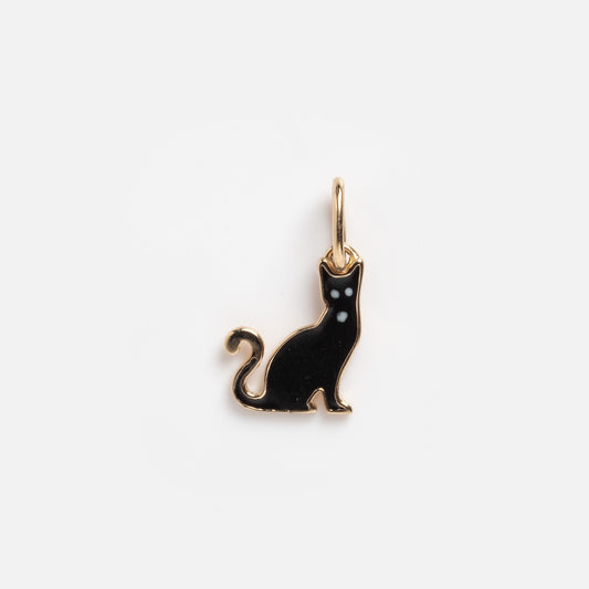 The Solid Gold Black Cat Charm Sample features a small black cat with white eyes, a curled tail, and a gold rim. It has a loop at the top for attaching to jewelry and is displayed on a plain white background.