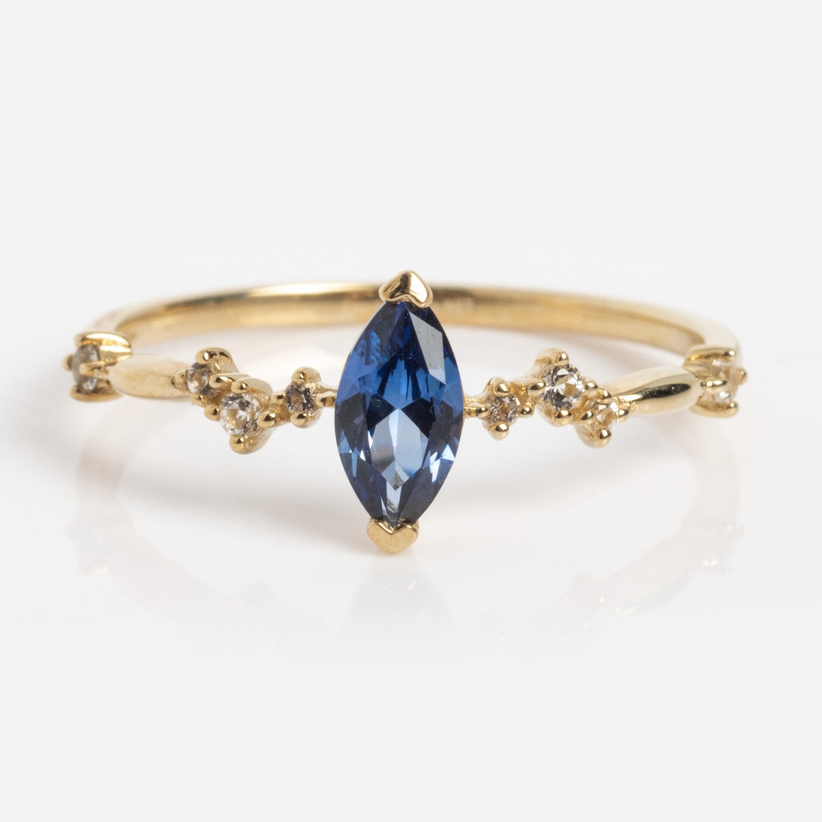 The Solid Gold Delicate Tanzanite Marquise Ring (Sample Size 7) features a marquise-cut lab tanzanite center with round white topaz clusters set in 9k yellow gold.
