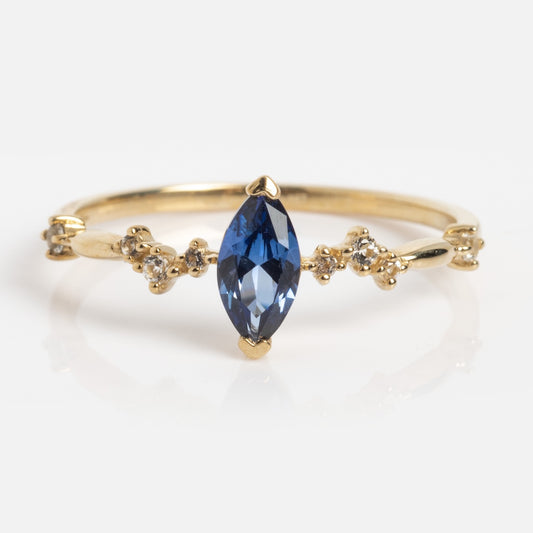 The Solid Gold Delicate Tanzanite Marquise Ring (Sample Size 7) features a marquise-cut lab tanzanite center with round white topaz clusters set in 9k yellow gold.