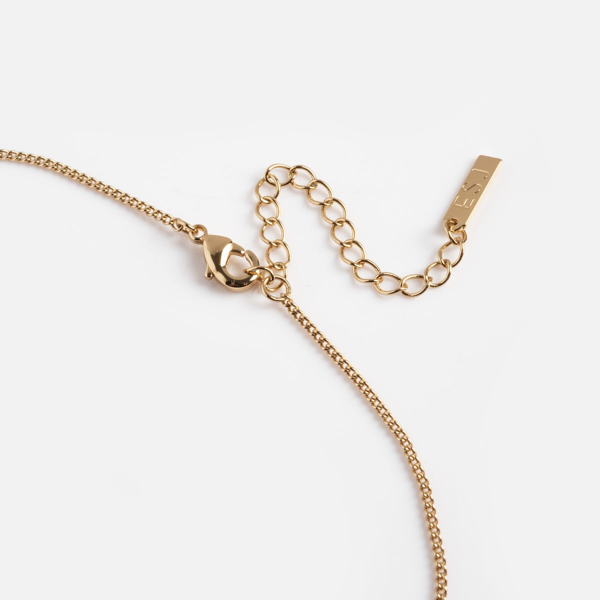 A close-up of the Stellina Pendant Necklace—a gold chain with a lobster clasp, adjustable extension, and a rectangular tag engraved with FELI—displayed on a white background.