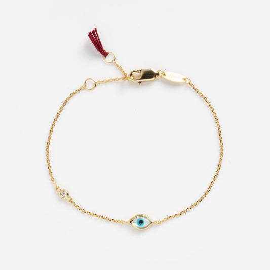 The Madison Evil Eye Bracelet is a delicate 14k vermeil piece with a blue evil eye charm, clear gemstone, lobster clasp, and burgundy tassel—blending stylish appeal with protective symbolism.