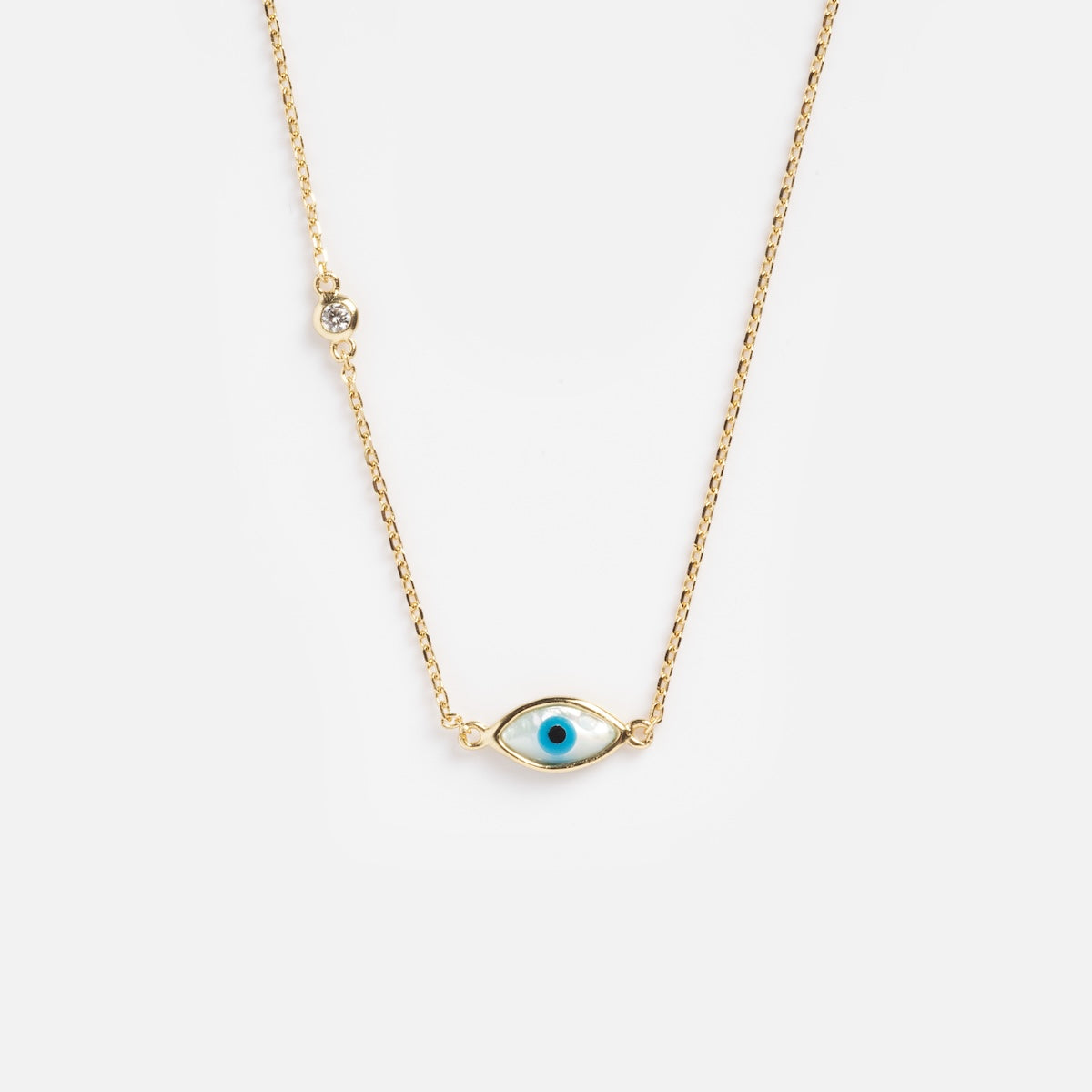 The Madison Evil Eye Necklace is a gold vermeil chain with an evil eye pendant, featuring a blue center and a sparkling cubic zirconia accent, shown against a plain white background.