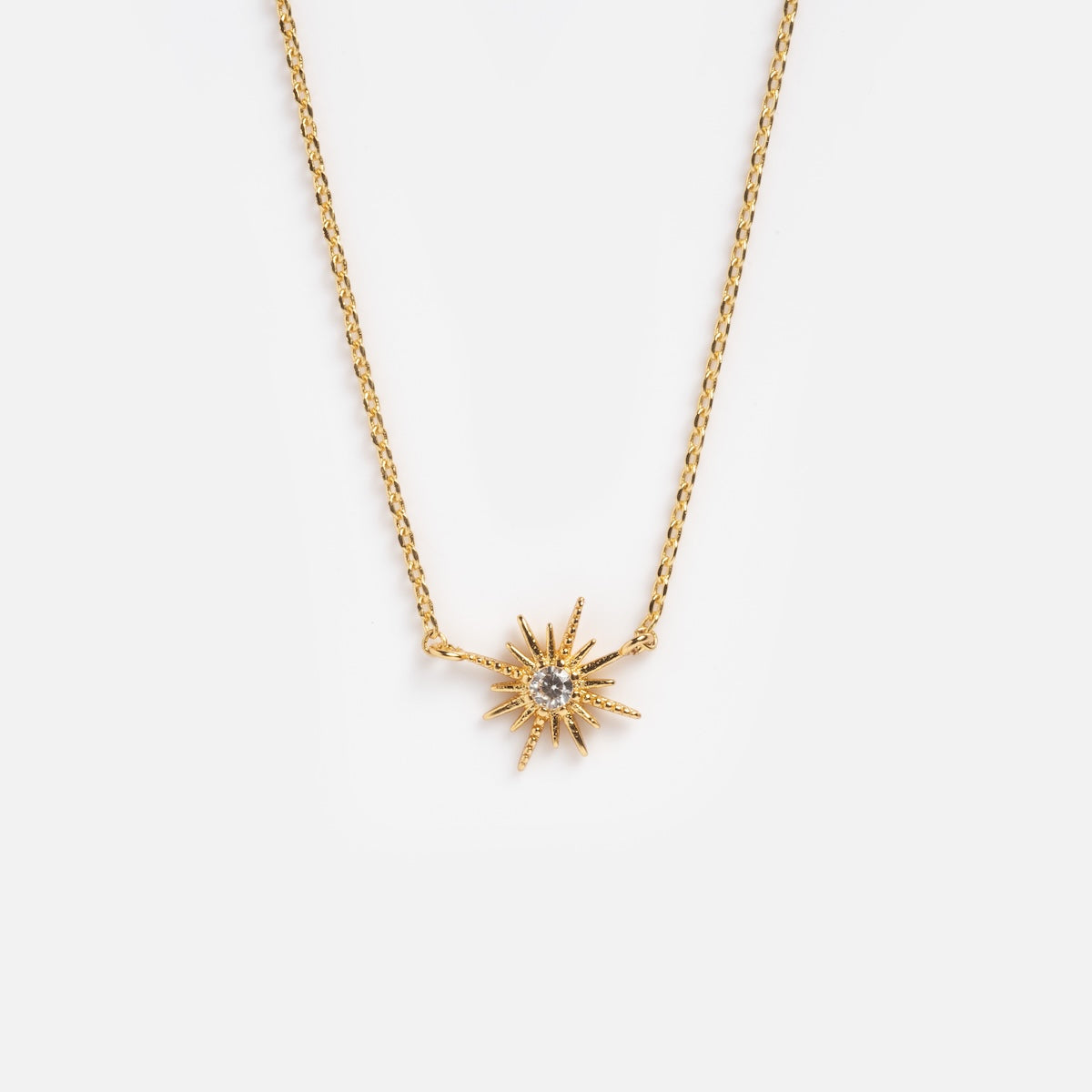 The Celestina Starburst Necklace showcases a sunburst-shaped gold pendant with sparkling cubic zirconia, displayed on a plain white background.