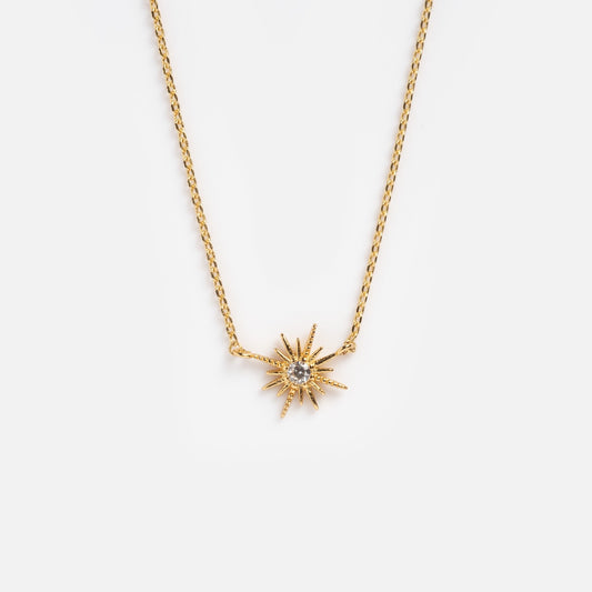 The Celestina Starburst Necklace showcases a sunburst-shaped gold pendant with sparkling cubic zirconia, displayed on a plain white background.