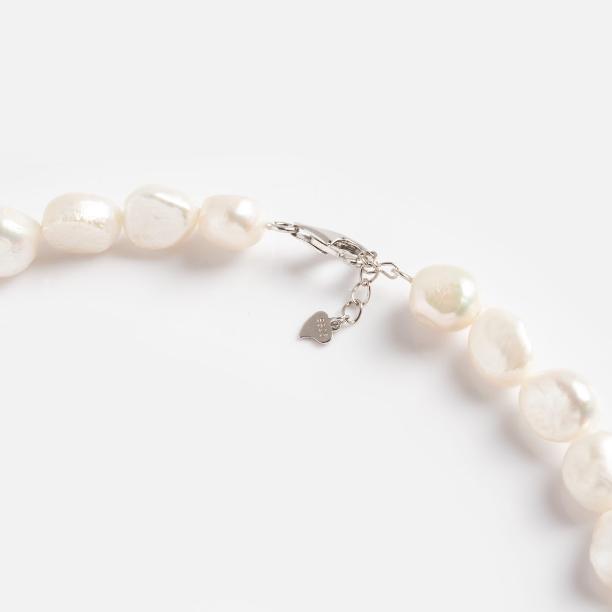A close-up of the La Fumee Necklace, showcasing irregular baroque white pearls with a silver clasp and a small heart-shaped charm, set against a plain white background.