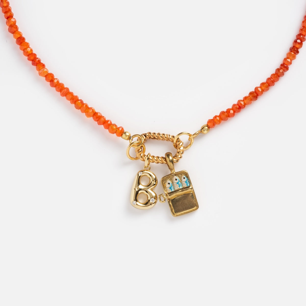 The Customizable Beaded Gemstone Charm Holder Necklace features orange beads, a brass knuckle gold charm, and a rectangular locket with blue and white floral detail—an eye-catching statement piece.
