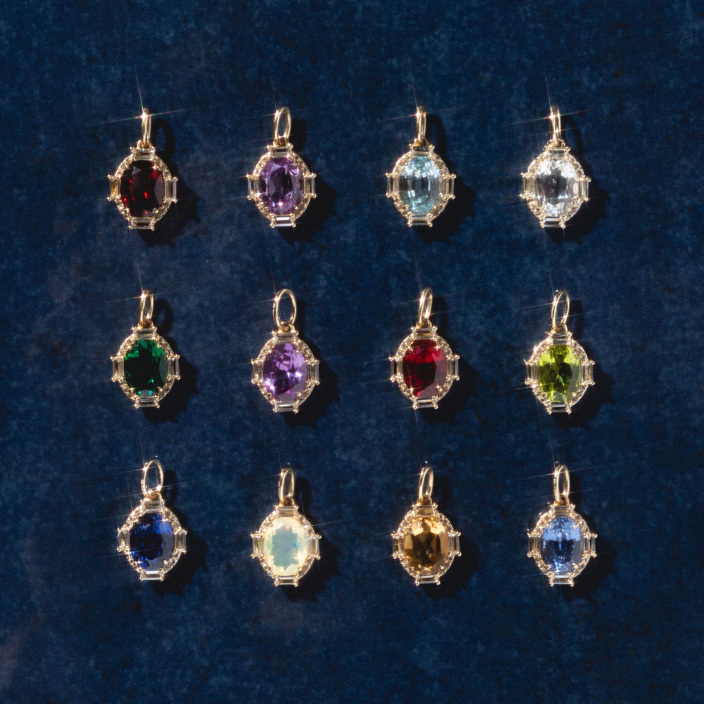 Twelve Solid Gold Vintage Inspired Birthstone Charms, each featuring a unique gemstone in a decorative gold frame, are arranged in a grid on a dark blue background.